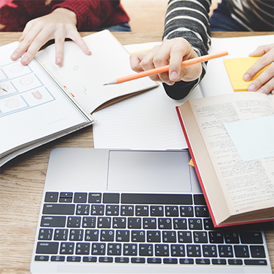 Two people working at a laptop, with books open.